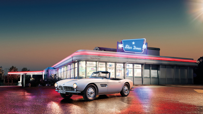 A white BMW 57 roadster parked outside an American diner at night time.